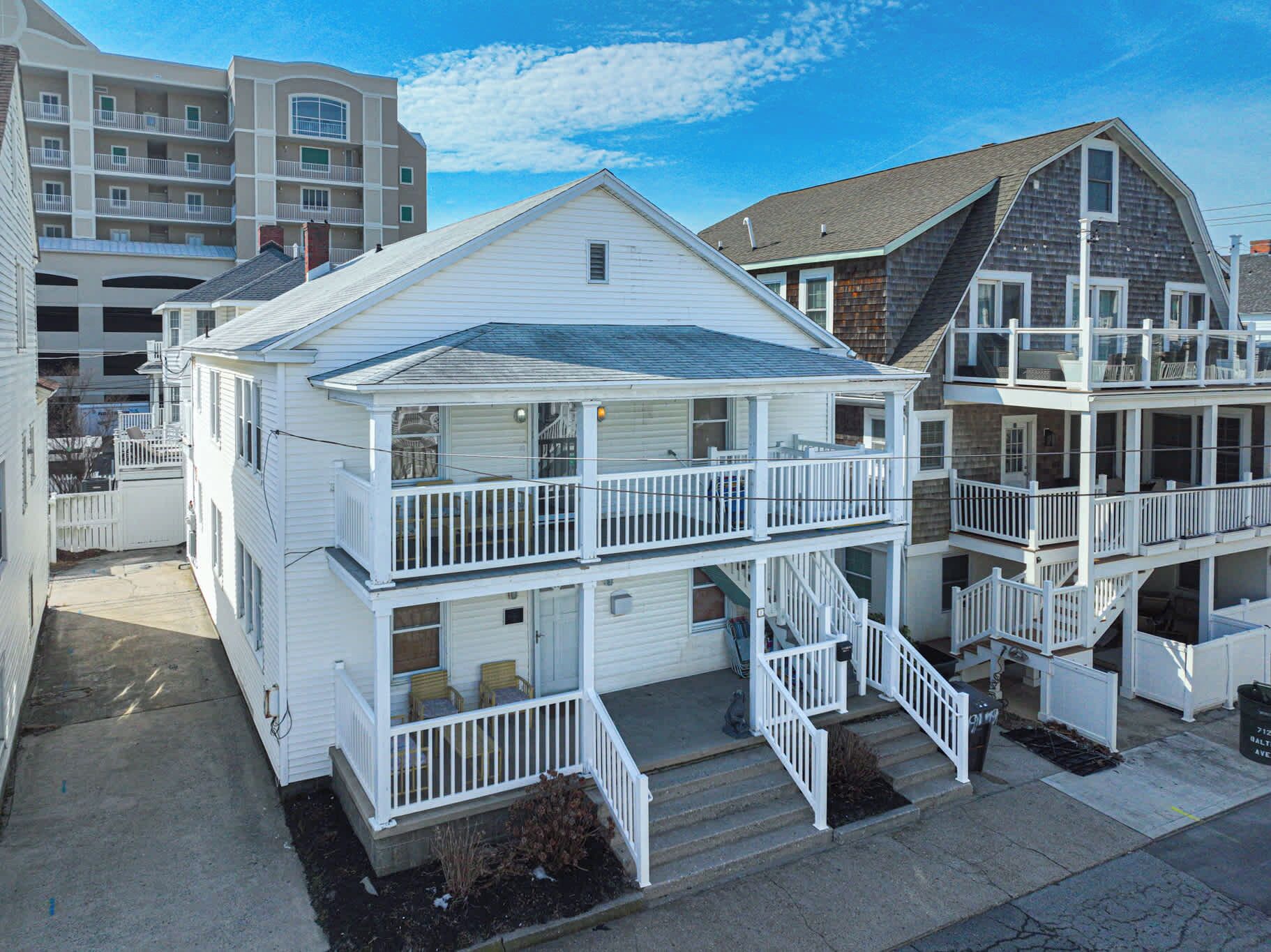 A two-story white beachfront house with a balcony and a small porch.
