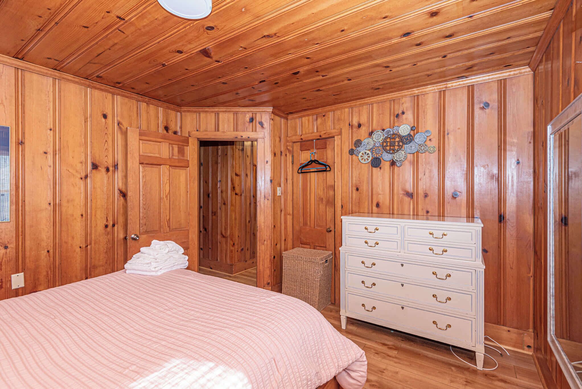 A wooden-paneled room with a bed, dresser, and a door leading to another room.