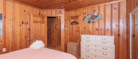 A wooden-paneled room with a bed, dresser, and a door leading to another room.