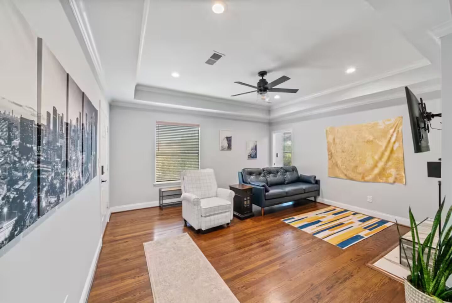 A modern living room with hardwood floors, a gray sofa, a white armchair, and a ceiling fan.