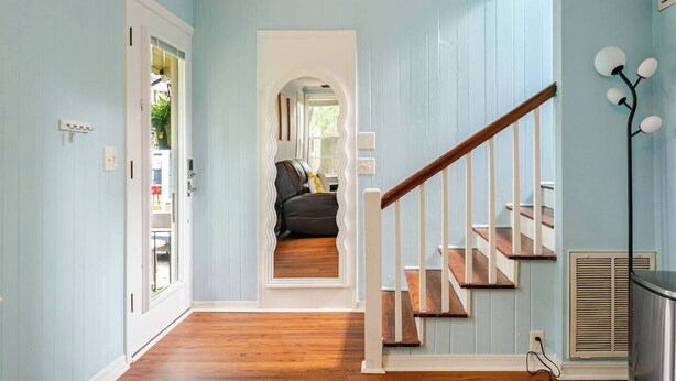 A hallway with a wooden staircase, a black leather sofa, and a white door.