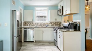 A modern kitchen with white cabinets, a stainless steel refrigerator, a dishwasher, a stove, and a microwave.