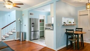A modern kitchen with a stainless steel refrigerator, a dining area with a wooden table and chairs, and a staircase leading to another level.
