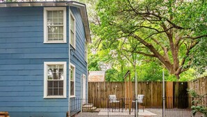 A blue house with a fenced backyard, a large tree, and outdoor seating.