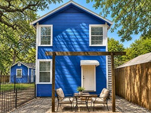A blue house with a porch, two windows, a door, and a small table with chairs.