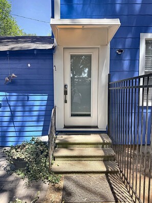 A house with a white front door, a small porch, and a black metal fence.