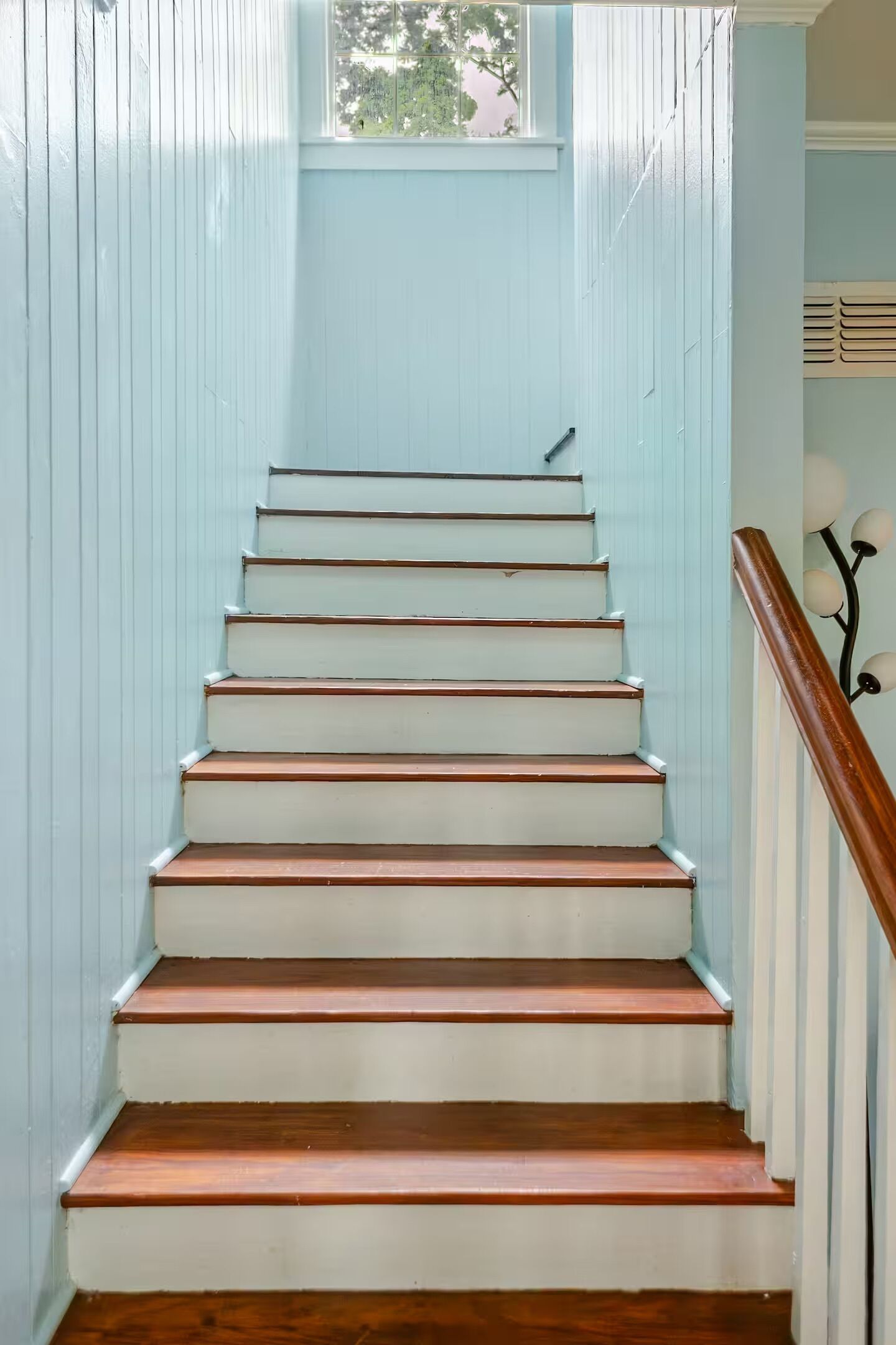 A staircase with wooden steps and white risers, leading to a landing with a window.
