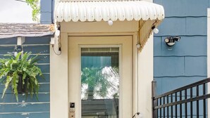 A house with a white door, a small porch with a white awning, a black metal gate, and a potted plant on the left.