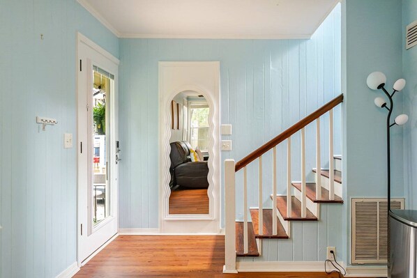 A hallway with a wooden staircase leading to an upper level, a door on the left, and a wall-mounted light fixture on the right.