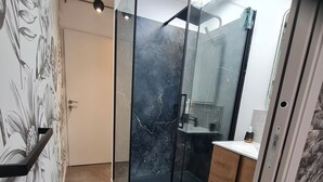 A modern bathroom with a glass shower enclosure, a marble backsplash, and a wooden vanity. - Nice little apartment (Pornic)