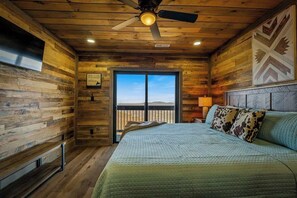 A room with a bed, a ceiling fan, a window with a view, and wooden walls. - 5-Bedroom Cabin with Indoor Pool, Pickleball Court & Hot Tub Near Dollywood (Sevierville)