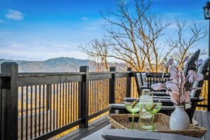 A deck with a view of mountains, a wicker table with drinks, and a vase with flowers. - 5-Bedroom Cabin with Indoor Pool, Pickleball Court & Hot Tub Near Dollywood (Sevierville)