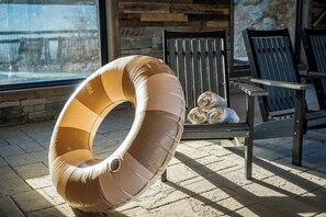 A lounge area with a unique circular chair, a bench with rolled-up towels, and a stone wall in the background. - 5-Bedroom Cabin with Indoor Pool, Pickleball Court & Hot Tub Near Dollywood (Sevierville)