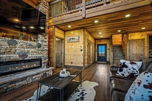 A spacious living area with a stone fireplace, wooden walls, and a leather couch. - 5-Bedroom Cabin with Indoor Pool, Pickleball Court & Hot Tub Near Dollywood (Sevierville)