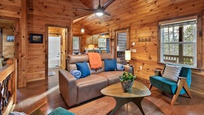 L’intérieur chaleureux d’un chalet avec un plafond en bois, un canapé en cuir, un coin repas et une grande fenêtre.