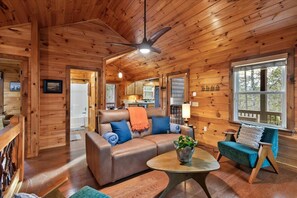 A cozy cabin interior with a wooden ceiling, a leather sofa, a dining area, and a large window. - Twig Hollow-Hot tub, fire pit, dog friendly, view (Mineral Bluff)