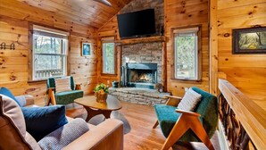 L’intérieur chaleureux d’un chalet avec des murs en bois, une cheminée en pierre et un téléviseur fixé au-dessus.