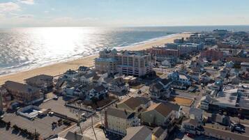 An aerial view of a coastal town with a beach, residential buildings, and a parking lot.