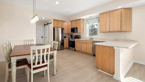 A modern kitchen with wooden cabinets, stainless steel appliances, and a dining area with a wooden table and chairs. - Newly Constructed Condo in the Heart of Ocean City (Ocean City)