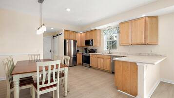 A modern kitchen with wooden cabinets, stainless steel appliances, and a dining area with a wooden table and chairs.