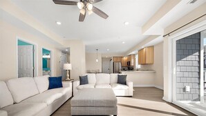 A spacious living room with a large white sofa, a grey ottoman, and a ceiling fan. - Newly Constructed Condo in the Heart of Ocean City (Ocean City)