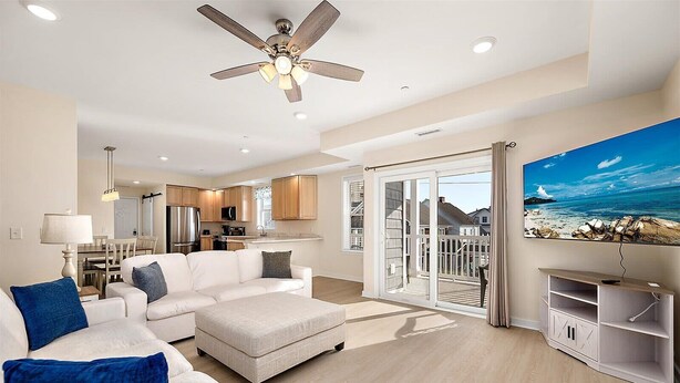 A modern living room with a white sofa, a flat-screen TV, and a balcony with a scenic ocean view. - Newly Constructed Condo in the Heart of Ocean City (Ocean City)