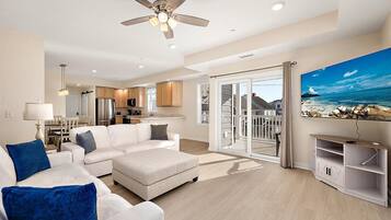 A modern living room with a white sofa, a flat-screen TV, and a balcony with a scenic ocean view.