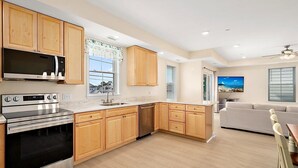 A modern kitchen with wooden cabinets, stainless steel appliances, a large window, and a view of the sea. - Downtown Condo Steps from the Beach and Boardwalk (Ocean City)