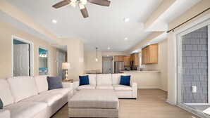 A spacious living room with a large sectional sofa, a coffee table, and a ceiling fan. - Downtown Condo Steps from the Beach and Boardwalk (Ocean City)