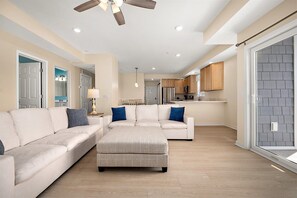 A spacious living room with a large sectional sofa, a coffee table, and a ceiling fan. - Downtown Condo Steps from the Beach and Boardwalk (Ocean City)