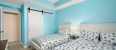 A bedroom with two beds, a ceiling fan, a nightstand with a lamp, and a door.