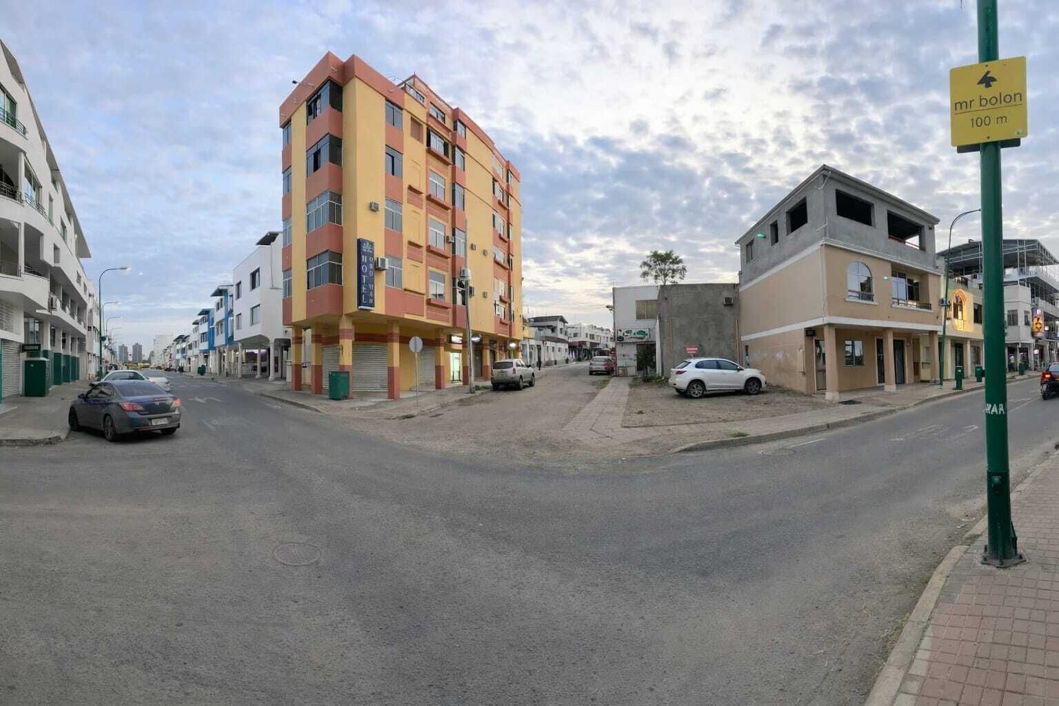 A multi-story hotel with a yellow and red facade, located at a street corner with parked cars.