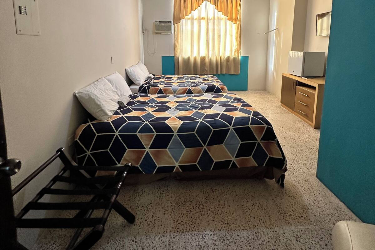 Un dormitorio con cama, escritorio, silla, armario y ventana con cortinas.