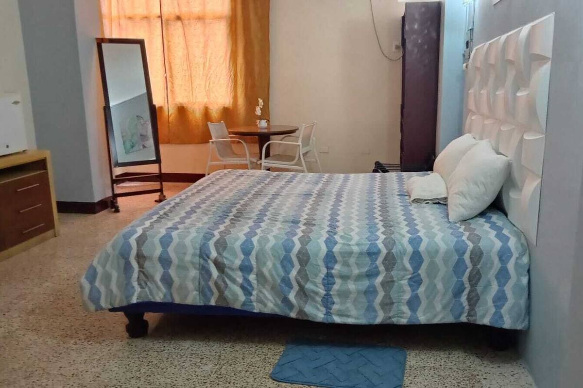 Un dormitorio con cama, una silla, una mesita y un espejo.