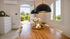 A dining area with a wooden table, white chairs, a black pendant light, and a vase with white flowers. - 🏡 Luxury Villa with Private Saltwater Pool – Porto ColumbuDiscover an exclusive oasis of luxury, privacy and relaxation in Porto Columbu, perfect for guests seeking a refined holiday in a modern and carefully designed villa.The property features a p (Sarroch)