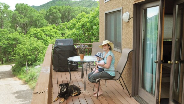 A deck with a table and chairs, a grill, and a dog lying on the deck.