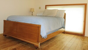 A wooden bed with a blue blanket and pillows, a bedside lamp, and a window with blinds.