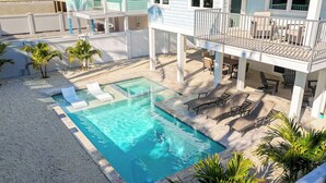 Uma piscina com espreguiçadeiras e área de deck, cercada por palmeiras e um muro branco.