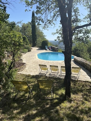 Une piscine dotée d’une plage en pierre, entourée d’arbres et offrant une vue sur le paysage.