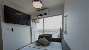 Ein modernes Schlafzimmer mit großem Fenster, Flachbildfernseher, Klimaanlage und einem Bett mit Kissen.