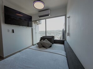 Ein modernes Schlafzimmer mit großem Fenster, Flachbildfernseher, Klimaanlage und einem Bett mit Kissen.