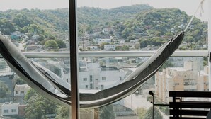 Eine Hängematte an einem Fenster mit Blick auf eine Stadtlandschaft, mit Gebäuden und Grünflächen.