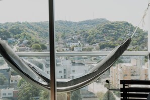 Eine Hängematte an einem Fenster mit Blick auf eine Stadtlandschaft, mit Gebäuden und Grünflächen.