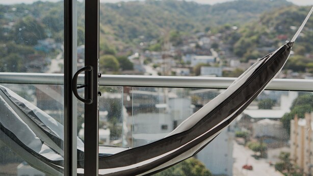 Eine Hängematte, befestigt an einem Balkongeländer, mit Blick auf eine Hügelstadt.