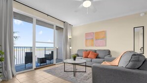 A spacious living room with a grey sofa, a round coffee table, and a balcony with a view. - Unique Disney & Lake view- 1BD condo (Orlando)