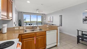 A modern kitchen with wooden cabinets, a built-in dishwasher, and a large window offering a view of the outdoors. - Unique Disney & Lake view- 1BD condo (Orlando)