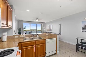 A modern kitchen with wooden cabinets, a built-in dishwasher, and a large window offering a view of the outdoors. - Unique Disney & Lake view- 1BD condo (Orlando)