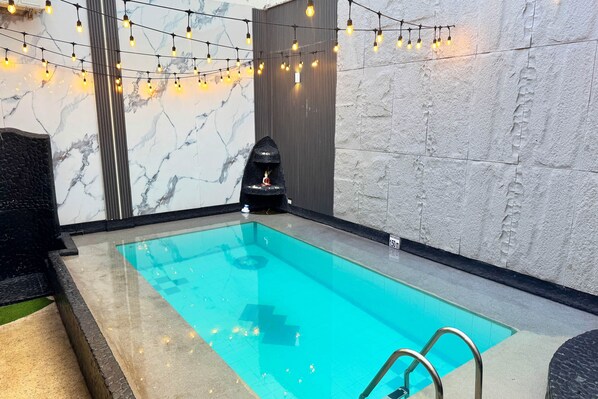A swimming pool with a clear blue water, surrounded by stone walls and a stone border.