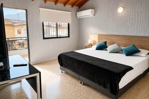A hotel room with a bed, a desk, a TV, a window with a view, and an air conditioning unit.