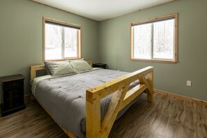 Ein Schlafzimmer mit einem Holzbettgestell, zwei Fenstern und einem Nachttisch.